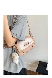 Detail of cream cat-shaped crossbody bag with plush bear charm worn by a model