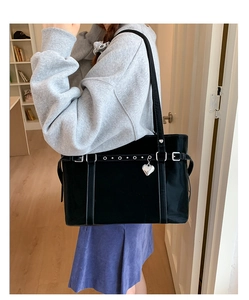 Close-up of a glossy black tote bag featuring a silver heart charm and belted buckle details