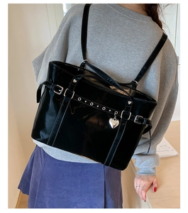 Detail of Y2K black patent leather bucket bag with heart pendant on shoulder