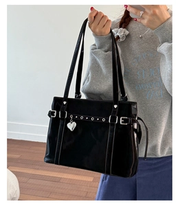 Close-up of glossy black tote bag with metallic heart charm and dual strap details