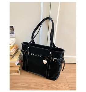 Detail of black patent leather bucket bag with silver buckles and a heart-shaped charm