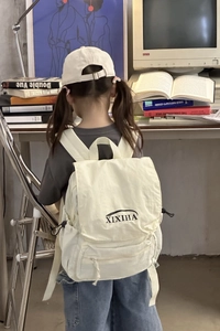 Detail of off-white canvas backpack showing side drawstring and brand logo in studio