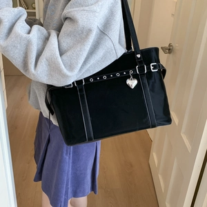 Detail of black tote bag featuring silver eyelet straps and heart pendant on shoulder