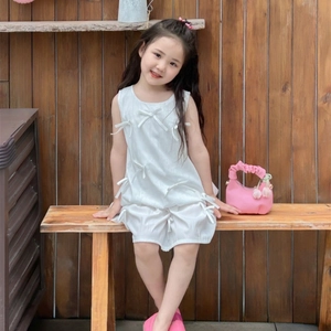 White sleeveless girl's dress with ribbon bows and pink accessories on a wooden bench