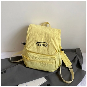 Detail of light yellow nylon backpack with XIXIHA logo on grey jacket background