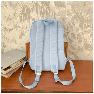 Détail du sac à dos en nylon bleu clair avec poches latérales brunes sur un bureau