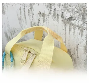 Detail view of the pale yellow children's bag featuring dual handles and a branded zipper