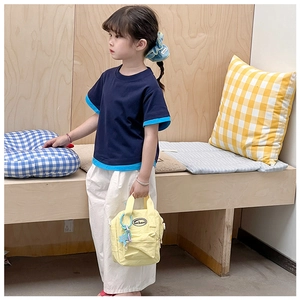 Detail of child carrying a mini yellow nylon messenger bag with blue logo tag