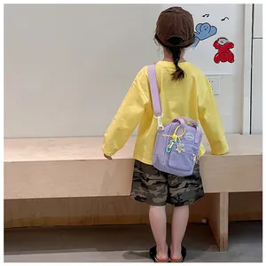 Detail of light purple canvas crossbody bag for kids with adjustable strap and colorful charms