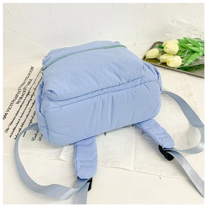 Close-up of a light blue puffy quilted backpack on a minimalist decorative surface
