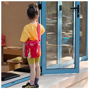 Detailed shot of kids red canvas crossbody bag with brand logo and colorful charm