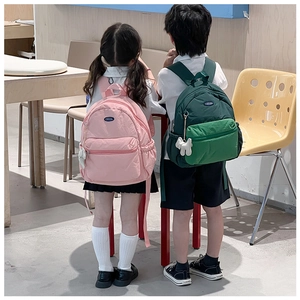 Detailed view of lightweight nylon kids backpacks in pink and green with cute plush charms