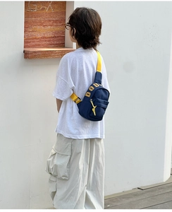 Detail view of navy canvas kids chest bag with yellow adjustable strap and doll pendant