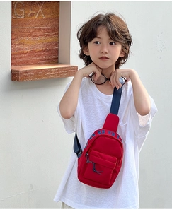 Close-up of a red kids crossbody bag with adjustable blue strap worn by a young boy