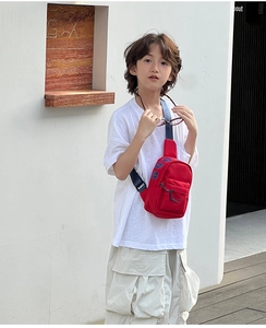 Outdoor shot of a kids red canvas crossbody chest bag with blue letter print and strap