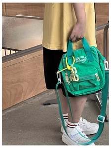 Close-up of green nylon crossbody bag for kids with decorative chains and white logo