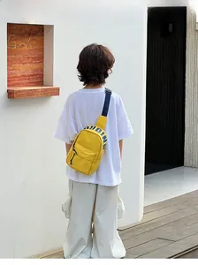 Detail of yellow canvas kids chest bag featuring PUDING logo worn by a child outdoors