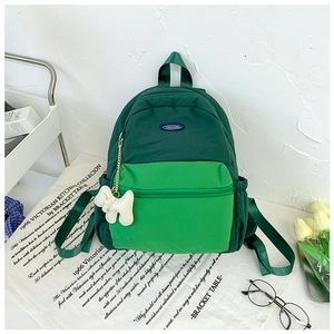 Close-up of green nylon children's backpack with cute white plush dog charm on table