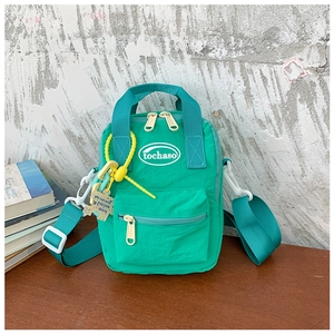 Detail of bright green kids crossbody bag with twin handles and a yellow puzzle charm