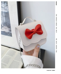 Detail of white girls' mini bag with red bow, wavy edges and silver chain strap