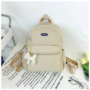 Detail view of beige nylon backpack with side drawstring pocket and cute plush charm