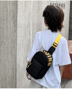 Close-up of black crossbody chest bag with yellow SPRING print and adjustable strap