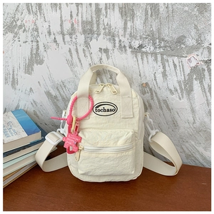 Detail view of cream mini crossbody bag with zipper pocket and pink puzzle charm accessory
