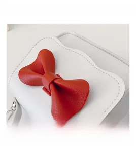 Close-up of white lychee leather texture and a large red bow on a mini crossbody bag