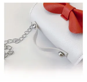 Close-up of white lychee leather mini bag with red bow detail and metal chain strap
