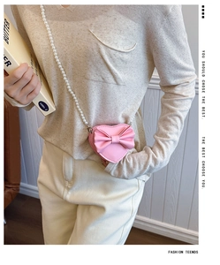 Close-up of pink heart-shaped girl's crossbody bag with bow detail and pearl chain strap
