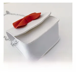 Close-up of white PU leather bag featuring red bow decoration and silver chain strap details