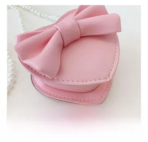 Detailed view of pink heart-shaped bag with leather bow and white pearl chain strap
