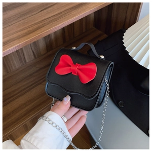 Detail of cute girls' mini handbag featuring a large red bow and silver chain strap