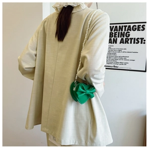 Detail of green heart-shaped kids bag with bow and pearl chain strap on a model