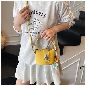 Detail of yellow woven bucket bag with doll pendant and pearl chain on a model