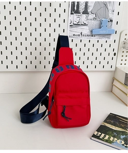 Detail of red nylon kids chest bag featuring navy blue zipper pull and strap accents