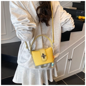 Detail of yellow woven crossbody bag with metal lock and a cute cartoon charm accessory