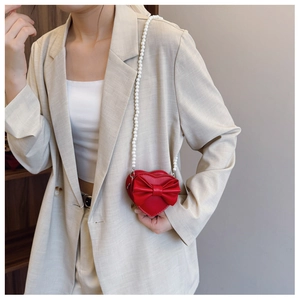 Detail of red heart-shaped girls crossbody bag with bow decoration and pearl chain