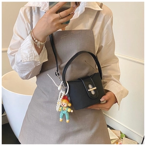 Detail of black mini bucket bag featuring a gold metal lock and a cute doll pendant charm