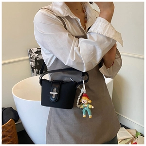 Detail of a mini black bucket bag with a cartoon doll pendant and pearl chain handle