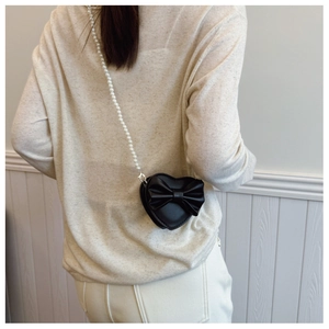 Detail of heart-shaped crossbody bag with bow accent and elegant pearl bead strap