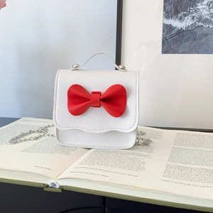 Mini girls white leather handbag with red bow detail and silver chain strap on a book