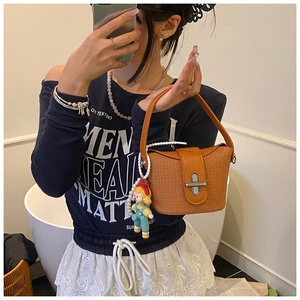 Close-up of woven orange bucket bag with leather flap, metal buckle, and cartoon charm