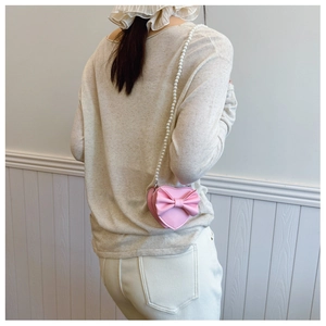 Pink heart-shaped girl bag with bow detail and white pearl chain strap in use