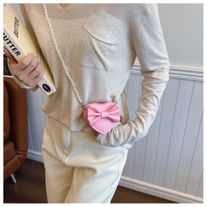 Close-up of pink heart-shaped mini crossbody bag with bow and pearl chain strap