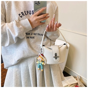 Detail of white textured crescent bucket bag with silver twist lock and doll charm