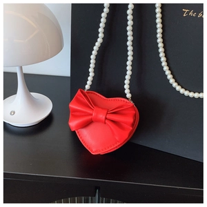 Close-up of a red heart-shaped kids purse with a large bow and white pearl chain strap