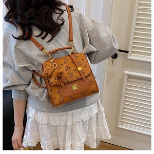 Détail d'un sac à dos marron style collège avec imprimés cartoon et breloque chat