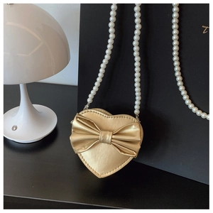 Close-up of golden heart-shaped bag with a 3D bow and elegant pearl chain strap