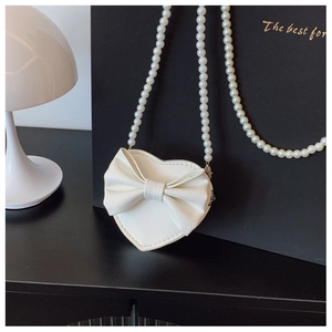 Detail of white heart-shaped bag featuring large bow and elegant pearl chain strap